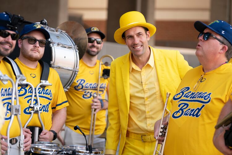 Jesse Cole, in a yellow suit and hat, poses with marching band musicians