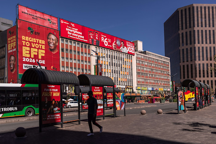 Billboards and bus shelters along a street at Gandhi Square, Johannesburg, including a large "Register to Vote EFF 2026 LGE" sign.