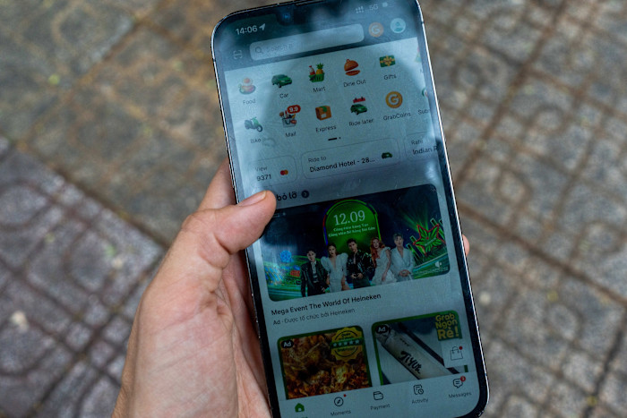A person holds a smartphone displaying the Grab app interface, showing ride-hailing and delivery options.