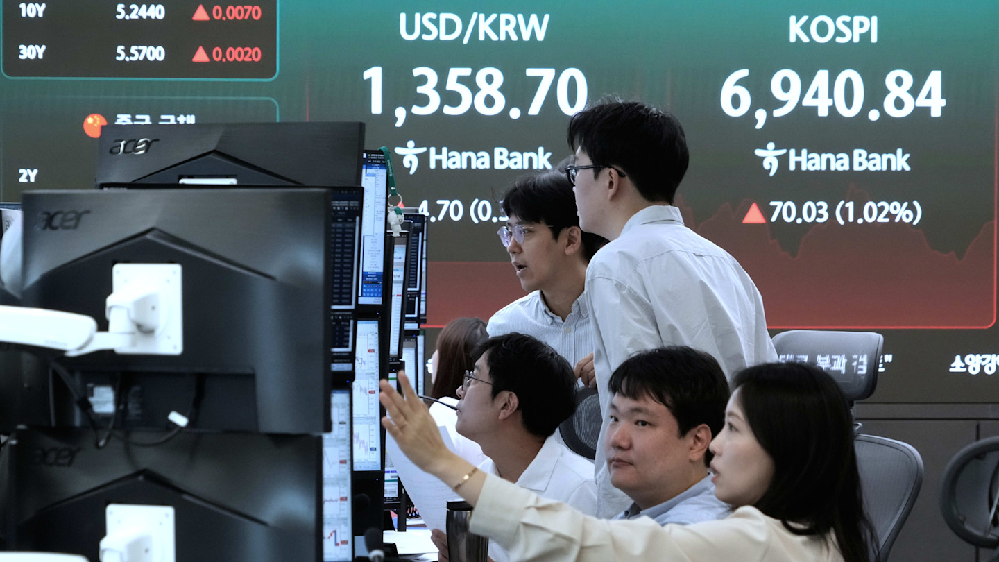 Currency traders work at computer stations in front of a large screen displaying the KOSPI index and USD/KRW exchange rate at Hana Bank.