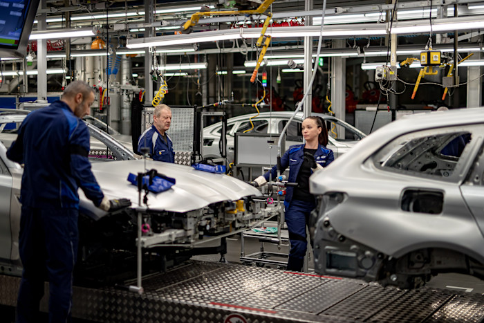 BMW manufacturing staff in blue uniforms inspect and work on unfinished car bodies at a factory assembly line