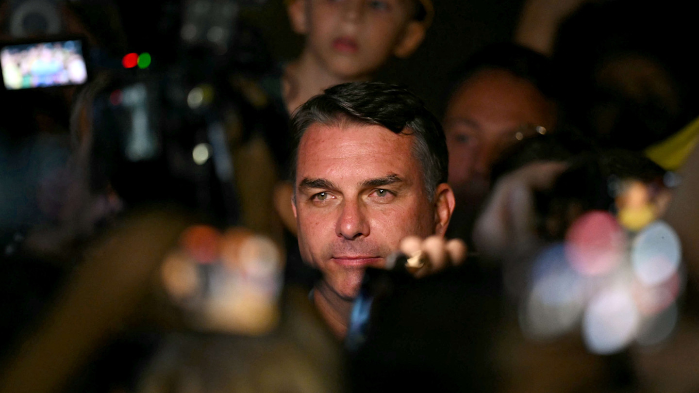 Flavio Bolsonaro looks ahead amid a crowd with cameras and blurred lights after the partial results of the presidential election.