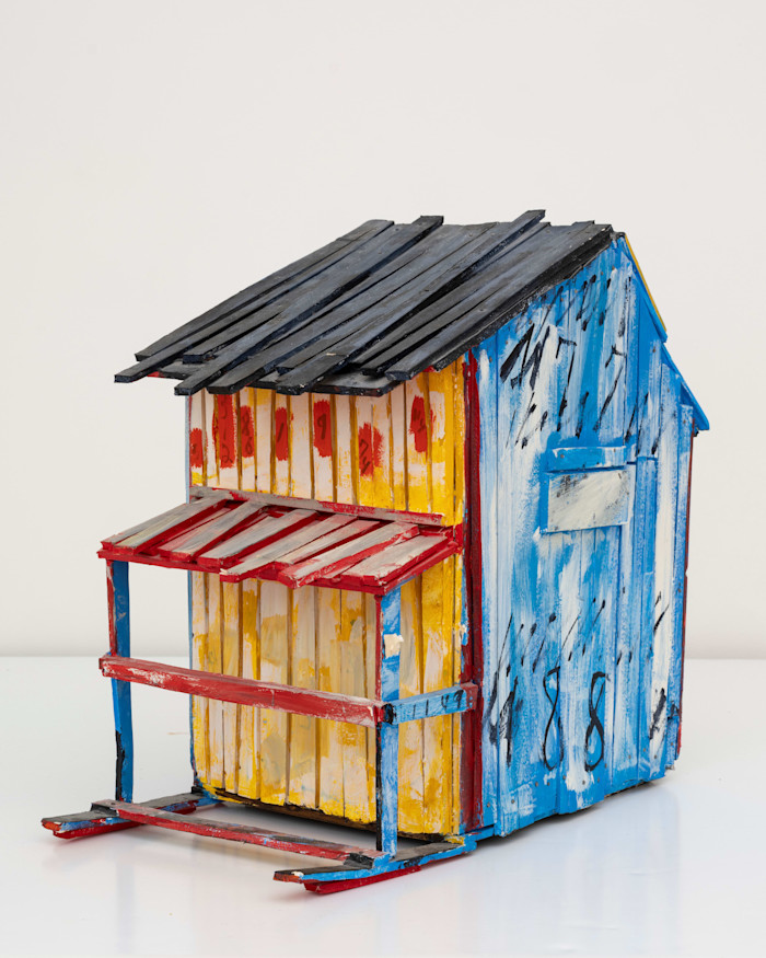 A miniature sculpture by Beverly Buchanan of a rickety shack made of wood and painted in blue, yellow and red with a little lean-to