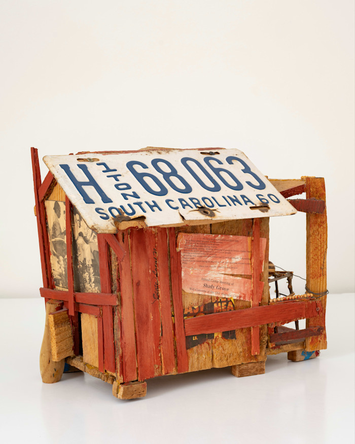 A miniature sculpture by Beverly Buchanan of a rickety shack made of different colour wood, red and yellow, and a South Carolina car licence plate used as the roof