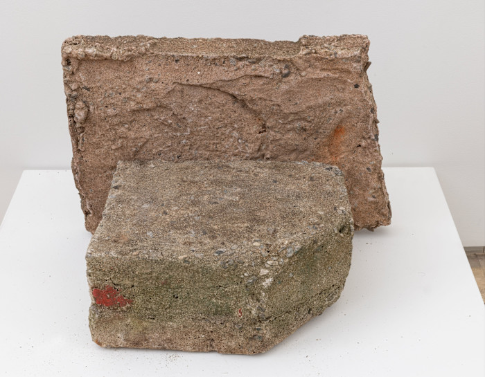 An abstract sculpture by Beverly Buchanan composed of two rough, rectangular cast concrete blocks with textured surfaces and patches of colour