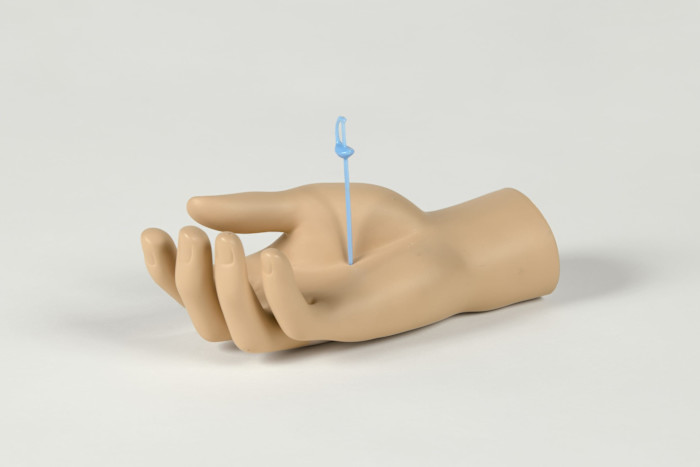 A realistic fibreglass hand by Alex Da Corte with a blue plastic stick piercing the palm and curving upward.