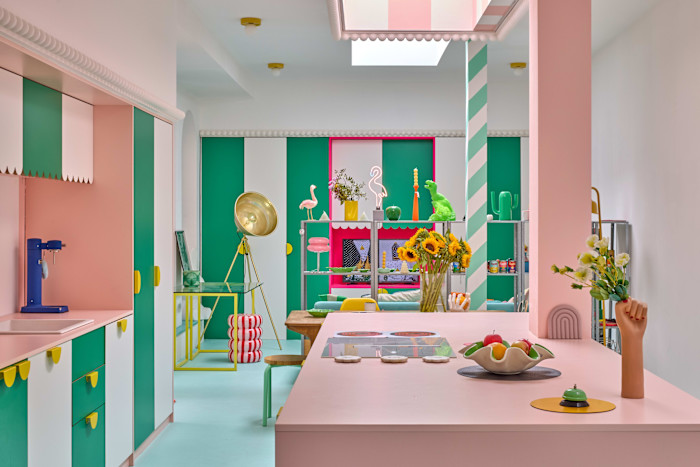 A kitchen and dining area with bold pink, green and white striped cabinetry and decor, playful objects and vases of flowers on the counter and table.