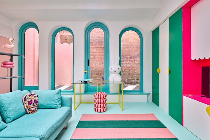 A brightly coloured living room with arched turquoise-trimmed windows, a teal sofa, striped rug and playful decor including a large white rabbit figure.