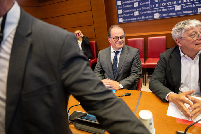 Emmanuel Moulin sits at a table during a Senate hearing, with two other people nearby and a "Commission des finances" sign in the background.