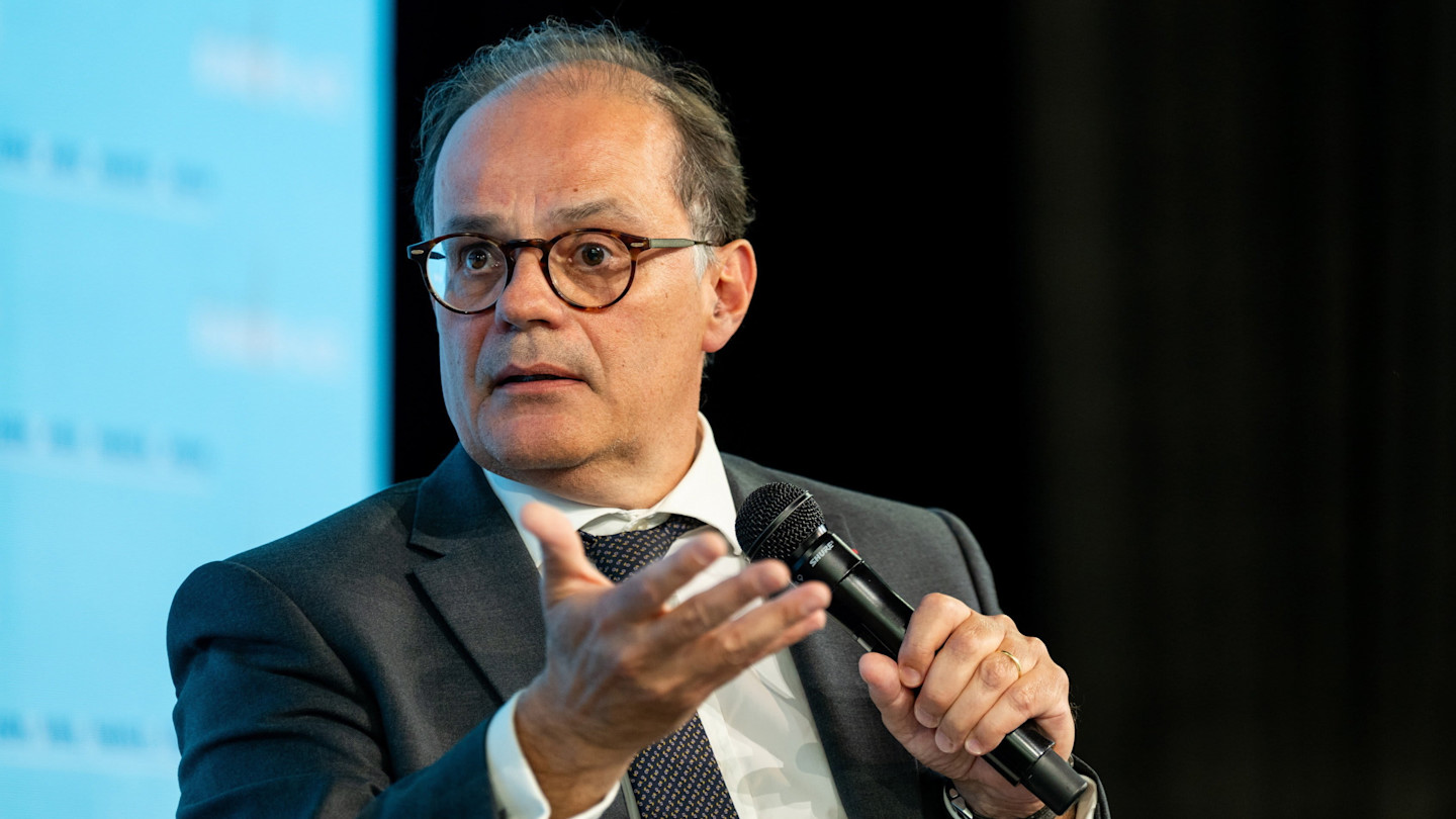 Emmanuel Moulin speaks while holding a microphone during the Paris Finance Forum.