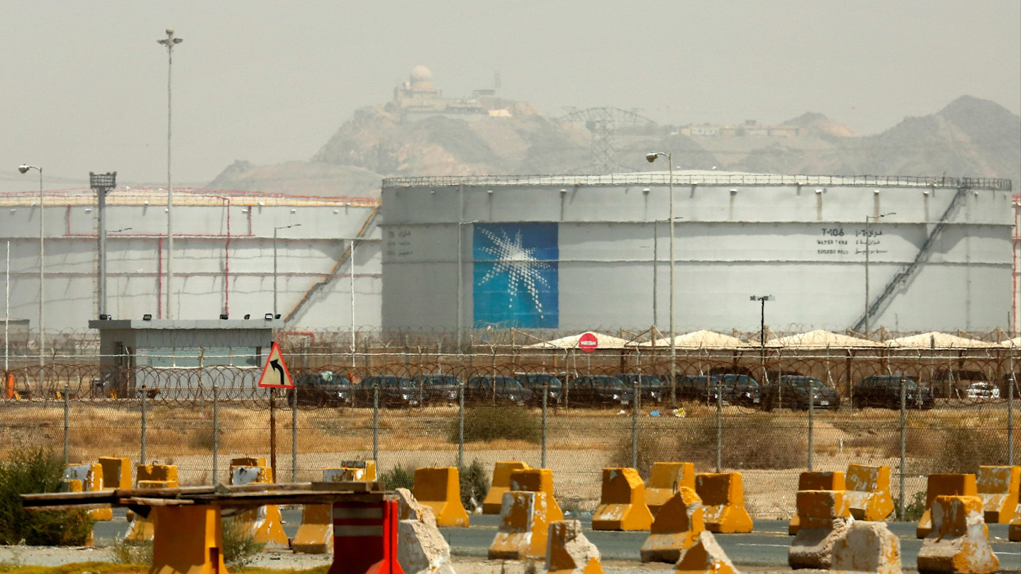 Large storage tanks at an Aramco oil facility, surrounded by fencing and security barriers.