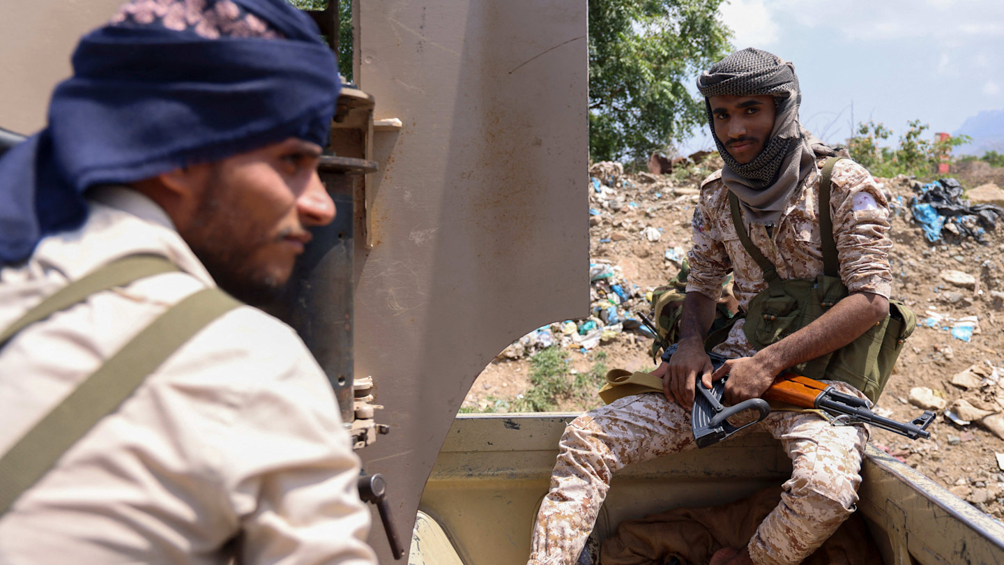 Two Yemen government soldiers sit in a military vehicle, one holding a rifle, near a front line west of Taiz.