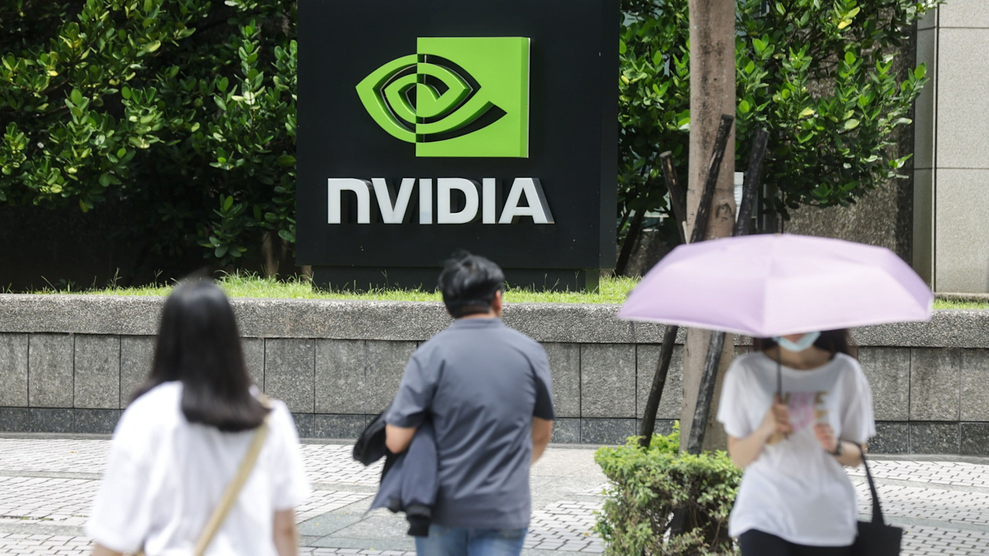 Nvidia’s logo and sign outside the company's Taipei office, with three people walking past, one holding a purple umbrella.