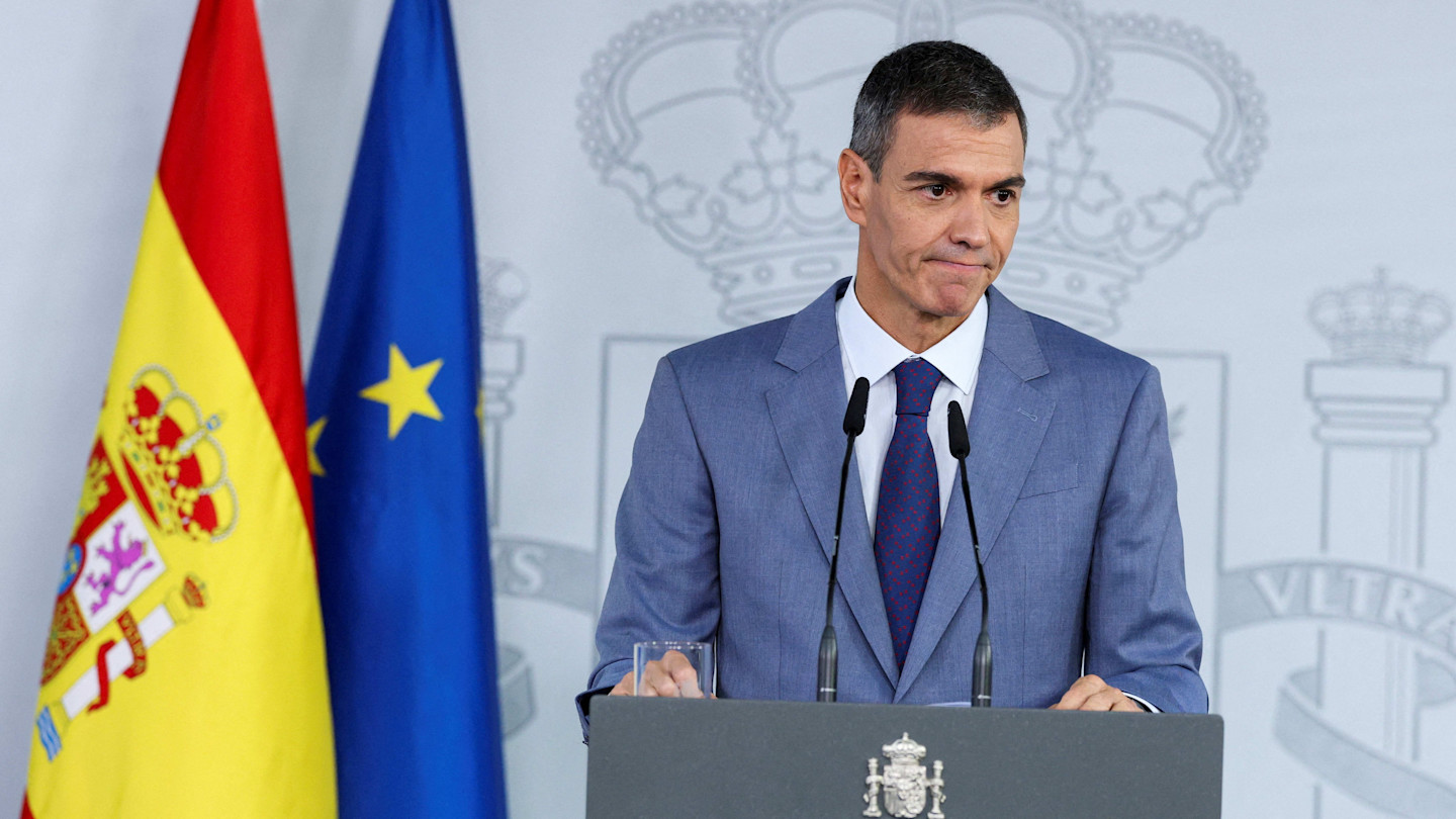 Pedro Sánchez stands at a lecture in front of the Spanish and EU flags