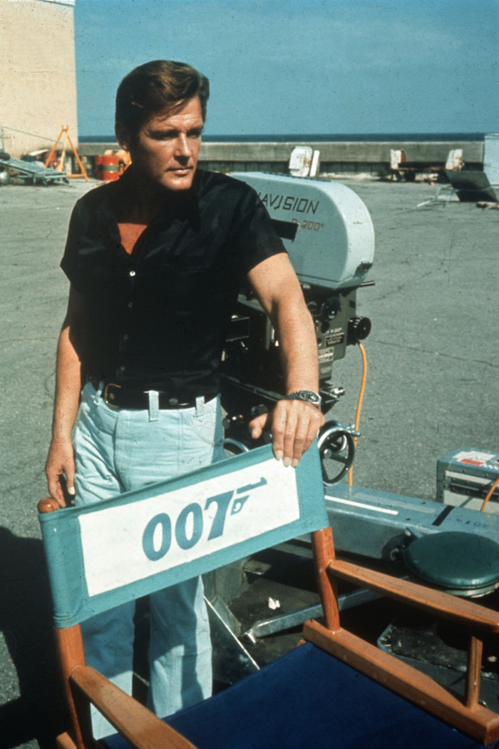 Roger Moore stands next to a director’s chair labeled "007" on the set of "Live and Let Die."