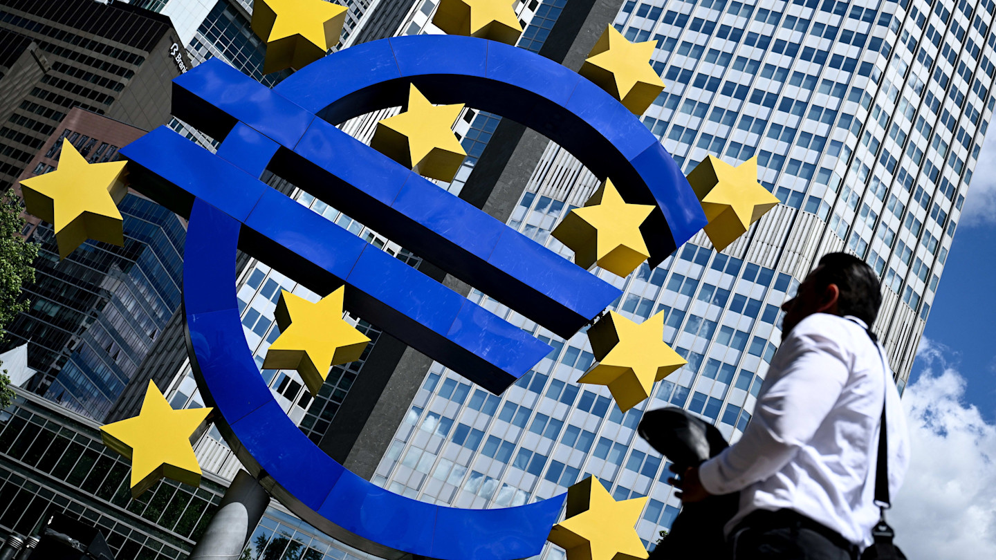 A man walks past the large blue and yellow euro currency sculpture in front of office buildings in Frankfurt.
