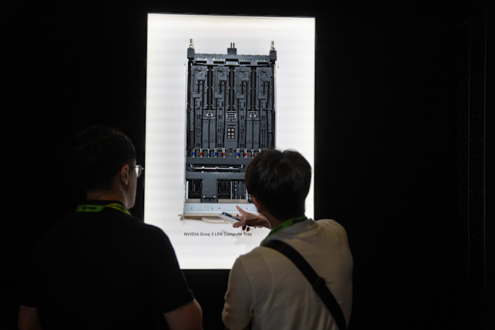 Two people look at a display of the Nvidia Groq LPX compute tray, with one pointing towards the hardware