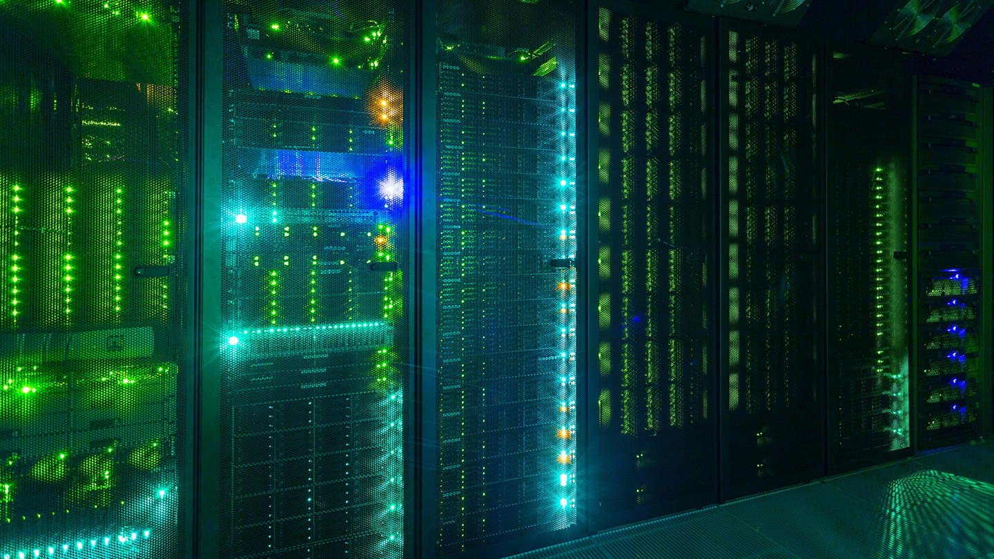 Rows of server racks with green and blue indicator lights illuminated in a data centre server room.
