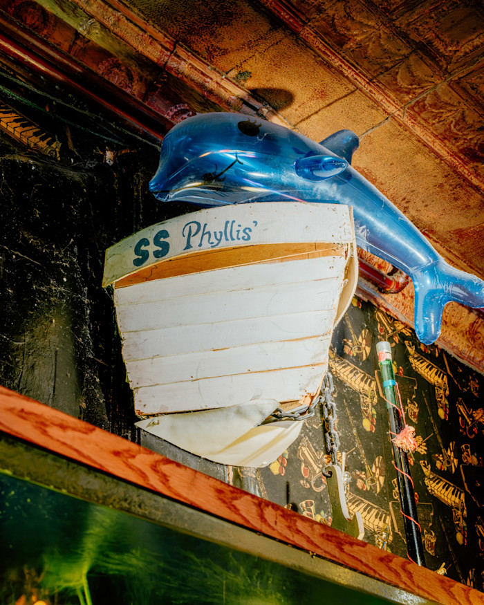 A wooden boat bow labeled "SS Phyllis'" is mounted on the wall with a blue inflatable dolphin above it.