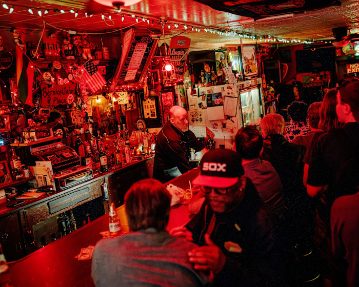 Steve Badauskas stands behind the bar at Bernice’s Tavern, serving drinks to patrons in a dimly lit, crowded bar.