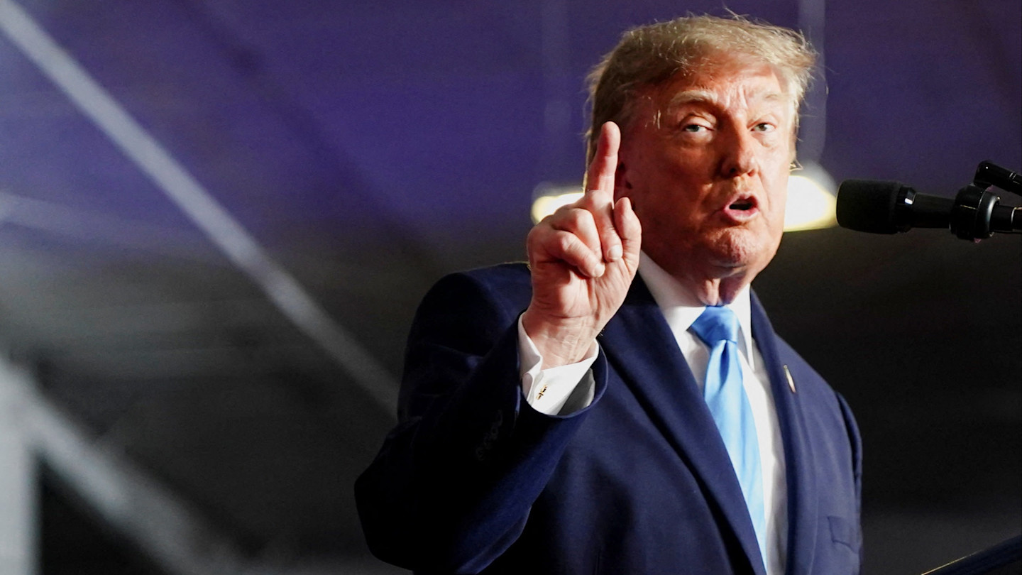 Donald Trump speaks at a microphone, holding up one finger during a rally.