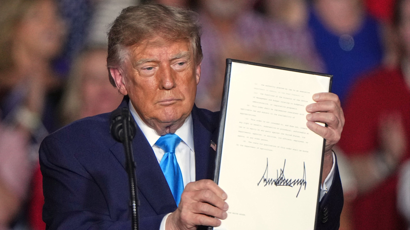 Donald Trump holds up a signed executive order, displaying the document and signature at a campaign rally.