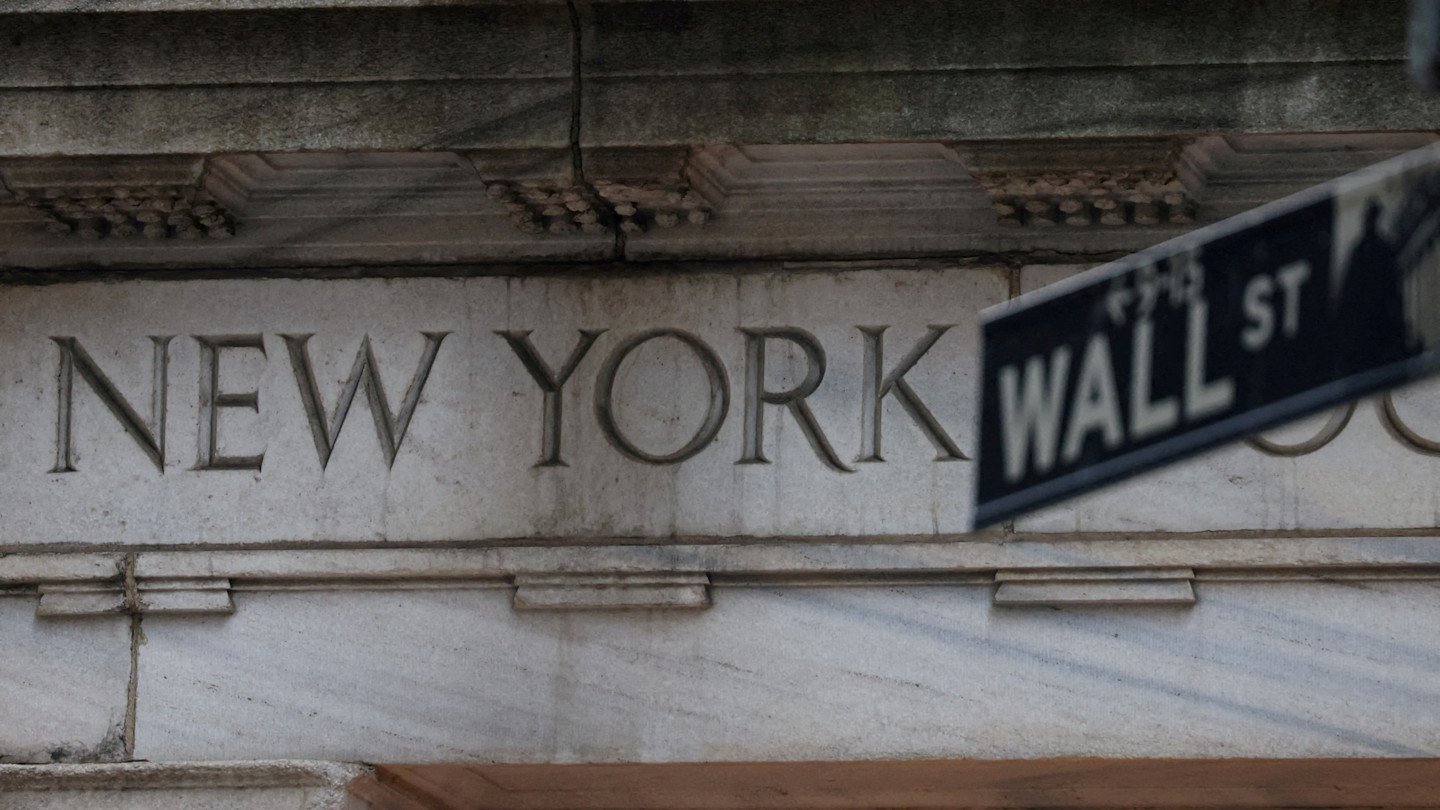 A Wall Street street sign is seen in front of the engraved "New York" lettering on the New York Stock Exchange building.