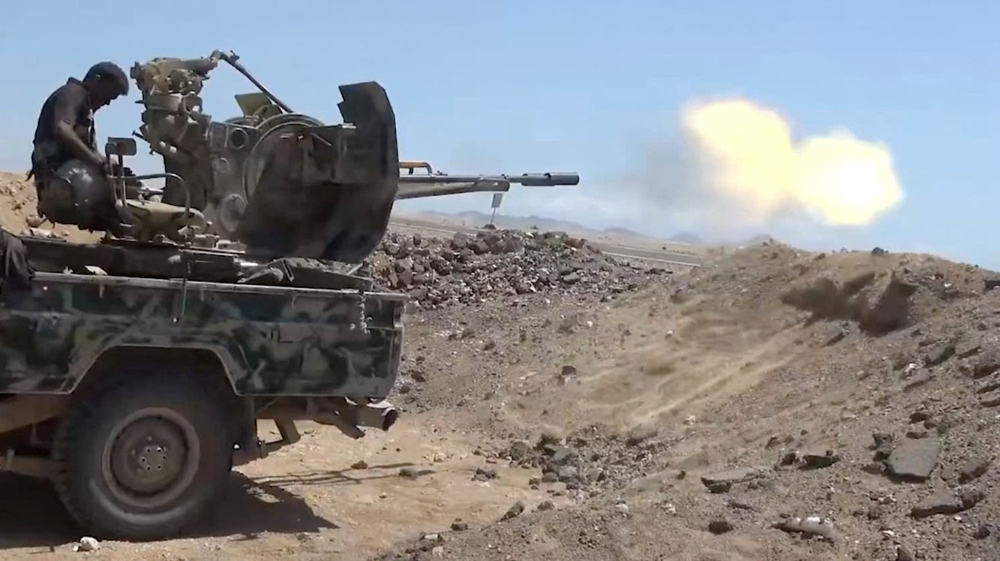 A pro-Saudi-backed Yemeni government fighter fires a large weapon mounted on a camouflaged vehicle in a rocky, desert area