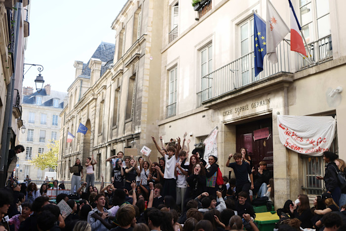 Students gathered in front of Lycée Sophie Germain, holding signs and cheering during a school blockade protest.