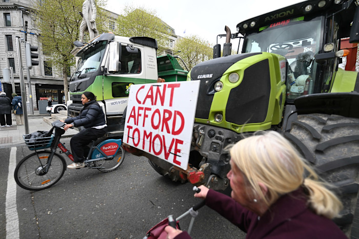 A tractor with a sign reading "CAN'T AFFORD TO MOVE" blocks the street as people pass by on foot and by bicycle during a fuel protest in Dublin.