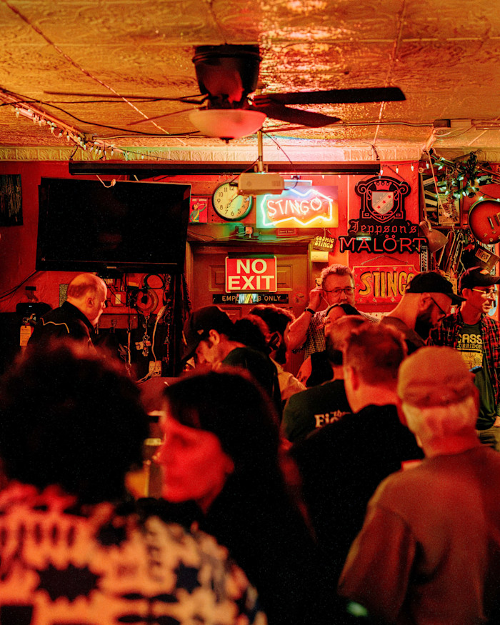 A crowded bar interior at Bernice’s Tavern with patrons gathered under warm neon lights and vintage signs on the walls.