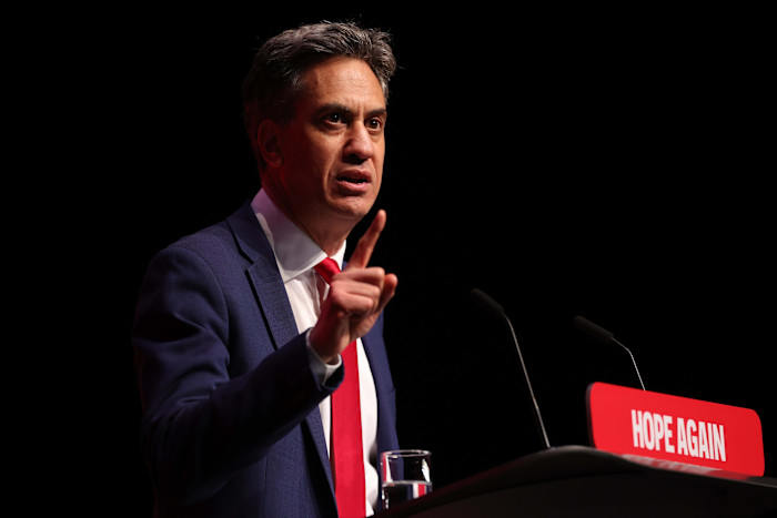Ed Miliband speaks at a podium labeled "Hope Again" during the Labour Party Conference, gesturing with his index finger raised.