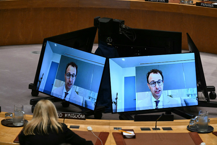 Dario Amodei appears on two large video screens during a UN Security Council meeting, with a delegate seated in front.