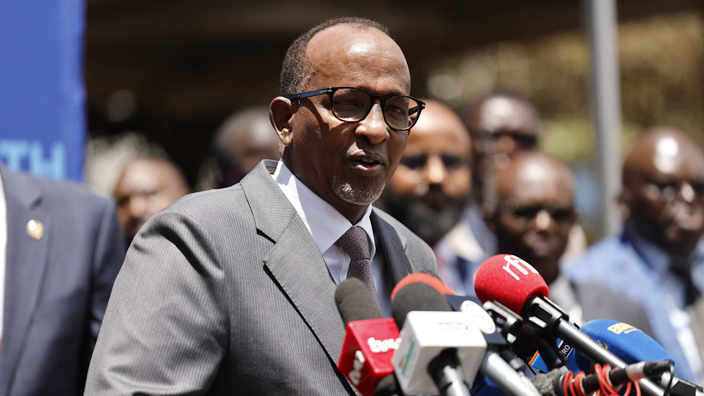 Aden Duale speaks at a press conference, standing behind several microphones, with people in suits in the background.