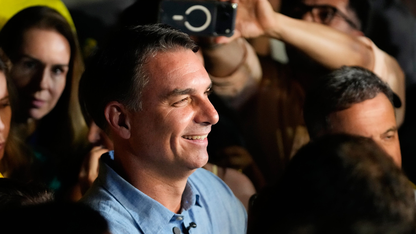 Flavio Bolsonaro smiles while speaking to supporters after advancing to a runoff election, surrounded by a crowd.