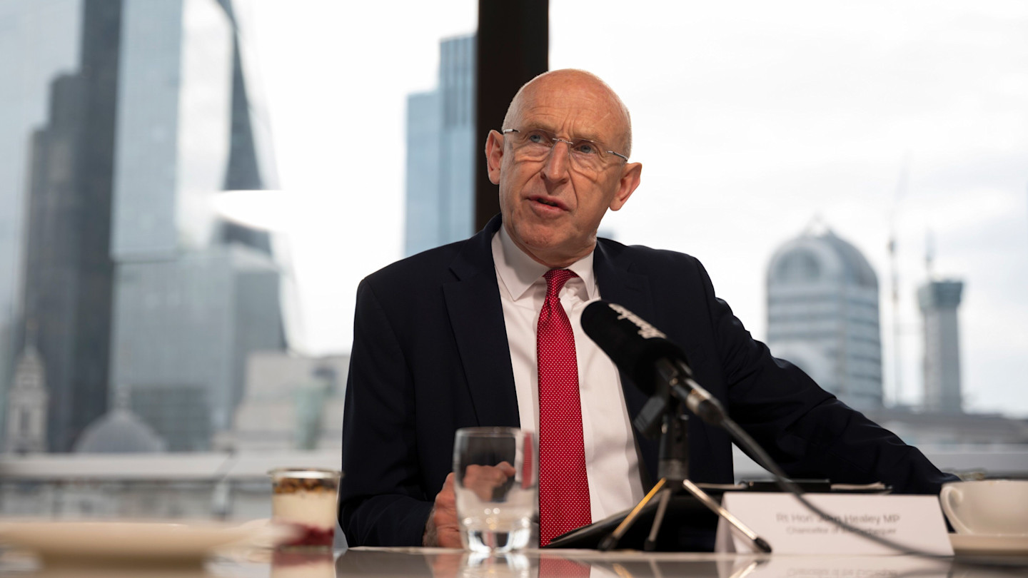John Healey, with City buildings visible through a window in the background,