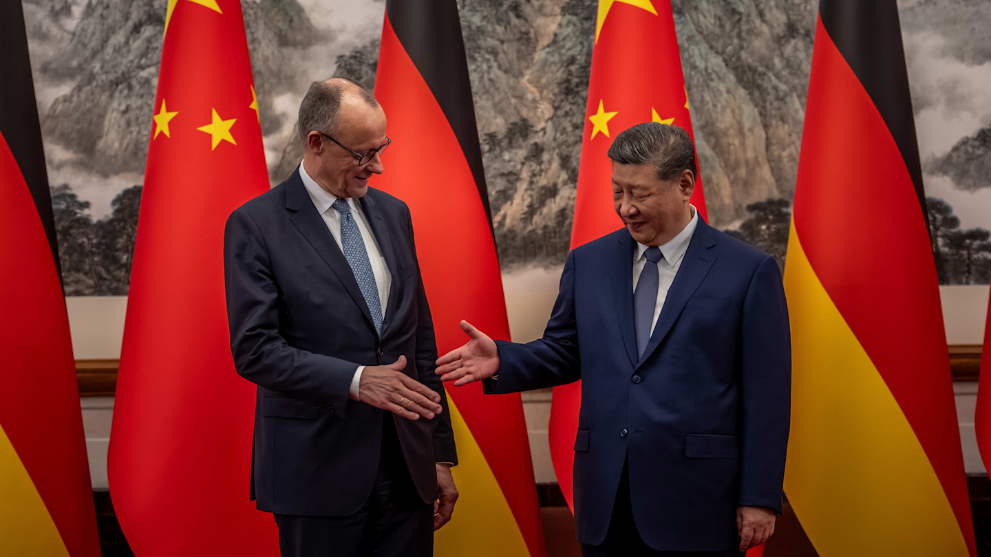 Friedrich Merz and Xi Jinping shake hands in front of German and Chinese flags at the State Guest House.