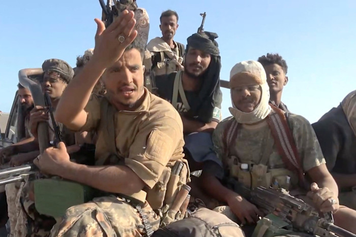 Several armed pro-Saudi Yemeni government fighters sit closely together in the back of a vehicle, some holding rifles