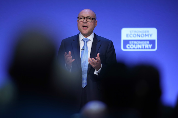 Andrew Griffith speaks on stage at the Conservative Party Conference, with a ‘Stronger Economy Stronger Country’ sign behind him.