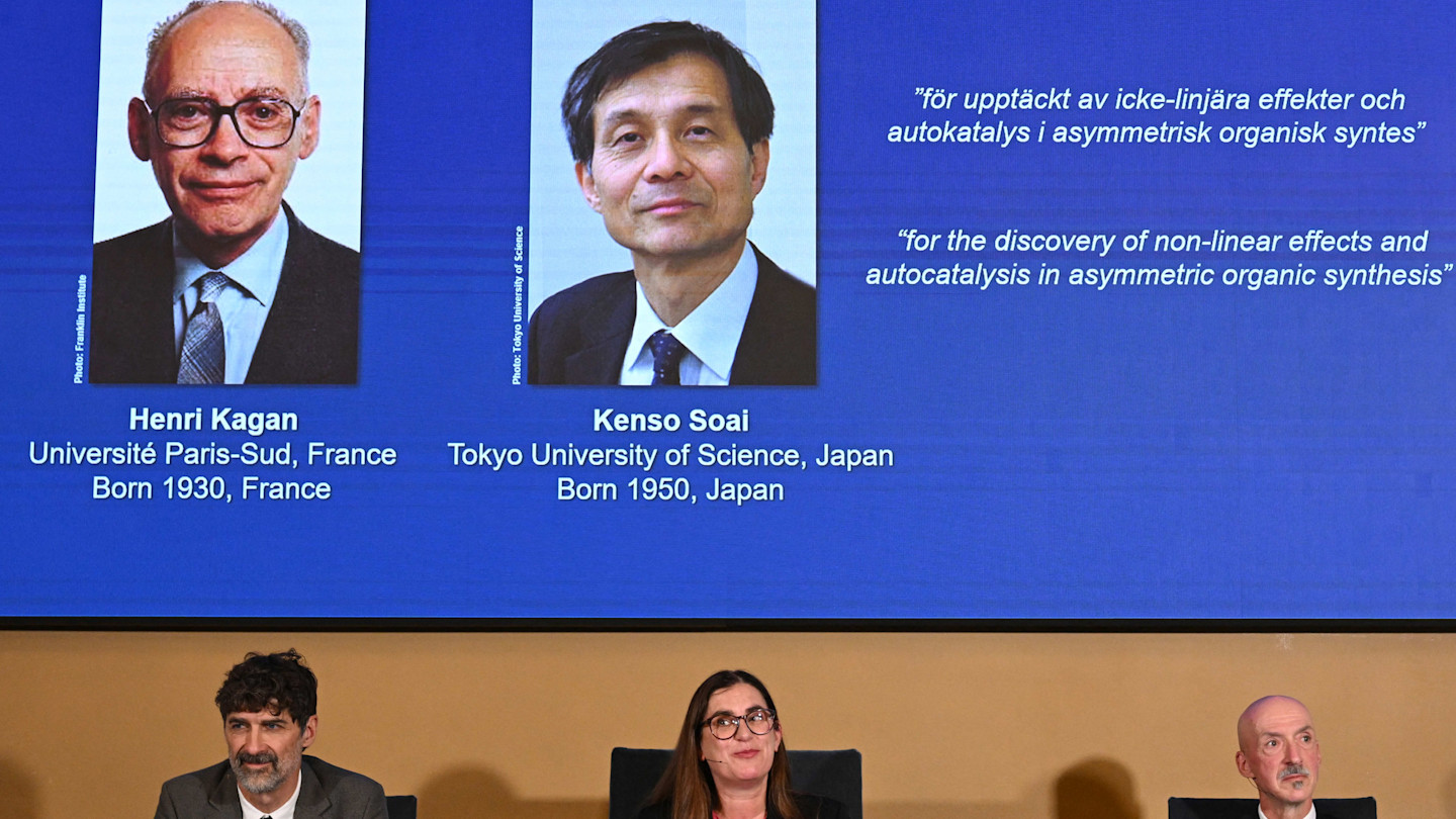 Heiner Linke, Ellen Moons and Peter Somfai react in front of a display announcing chemistry Nobel laureates Henri Kagan and Kenso Soai.