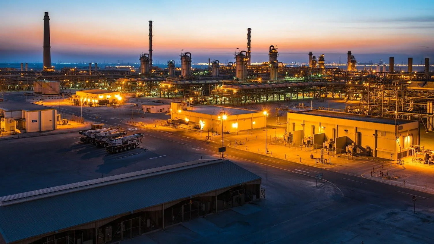 Alt text: Industrial gas processing facilities at the Jafurah Gas Field illuminated at dusk, with tall towers and buildings.