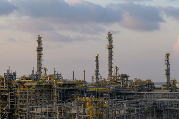 Several tall distillation towers and complex piping structures at the Jafurah gasfield, with a cloudy sky in the background.