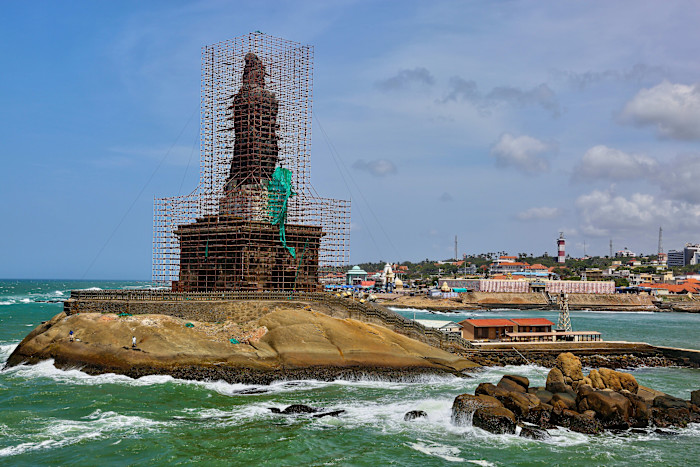 The statue of Thiruvalluvar in Kanyakumari covered in scaffolding during restoration work, with the sea and town in the background