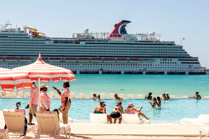 Guests relax in a lagoon pool under striped umbrellas as the Carnival Vista cruise ship is docked at Celebration Key.