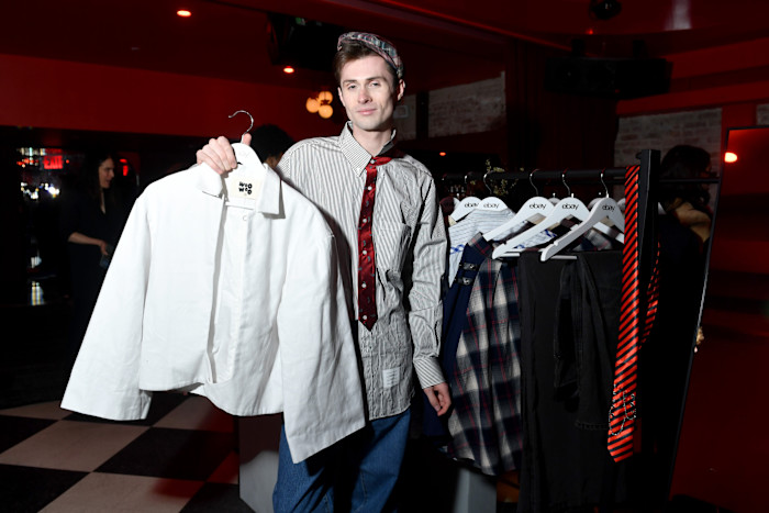 Dylan Kelly holds up a white shirt on a hanger next to a clothing rack with various garments at an eBay event.