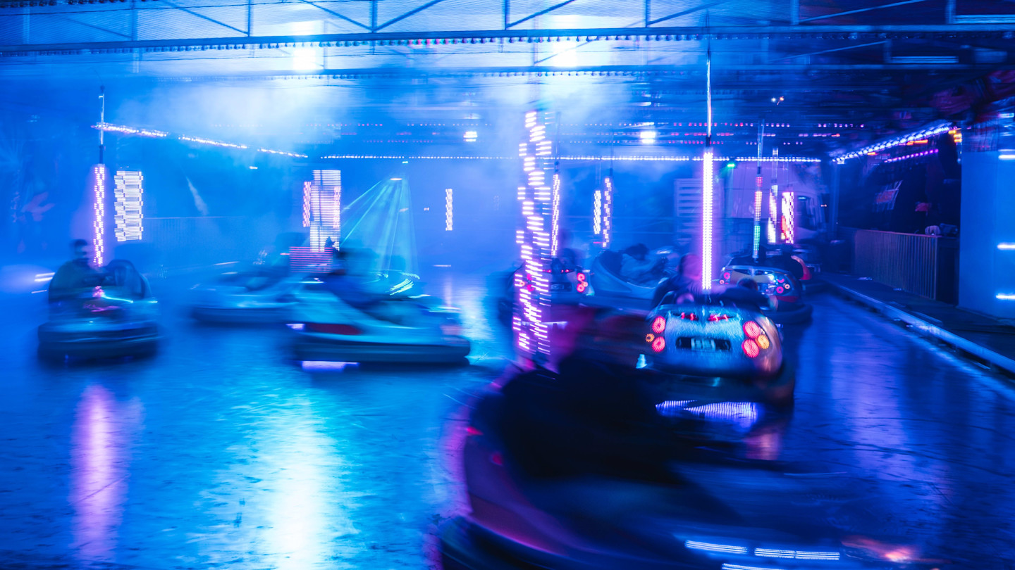 Dodgem cars in motion under blue and purple lights with blurred riders and illuminated poles.