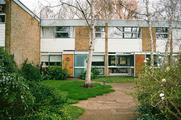 Two-storey mid-century modern terraced houses with large windows and a central courtyard garden with trees and shrubs.