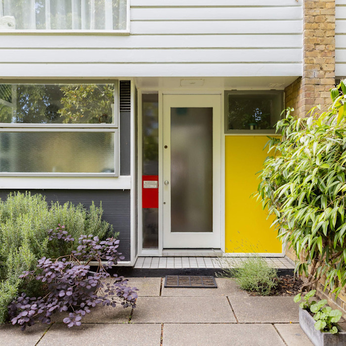 Modernist house entrance with frosted glass door, a large yellow panel and surrounding greenery. On the market with The Modern House.