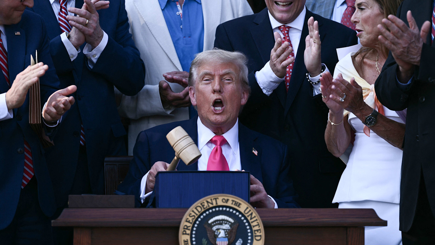 Donald Trump holds a gavel and speaks at a desk with the presidential seal, surrounded by applauding people.