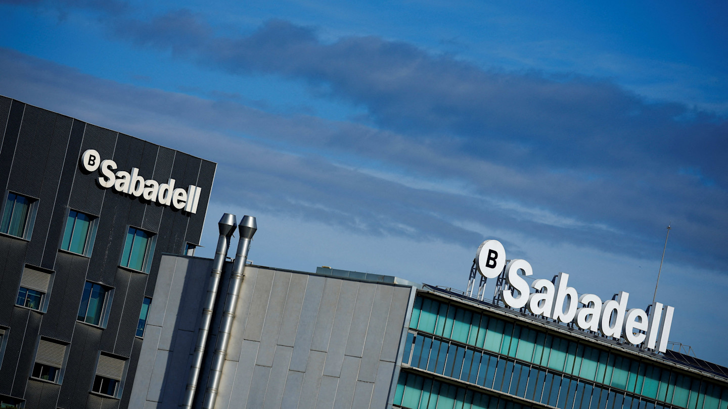 Sabadell bank logos on the rooftops of two office buildings under a partly cloudy sky.